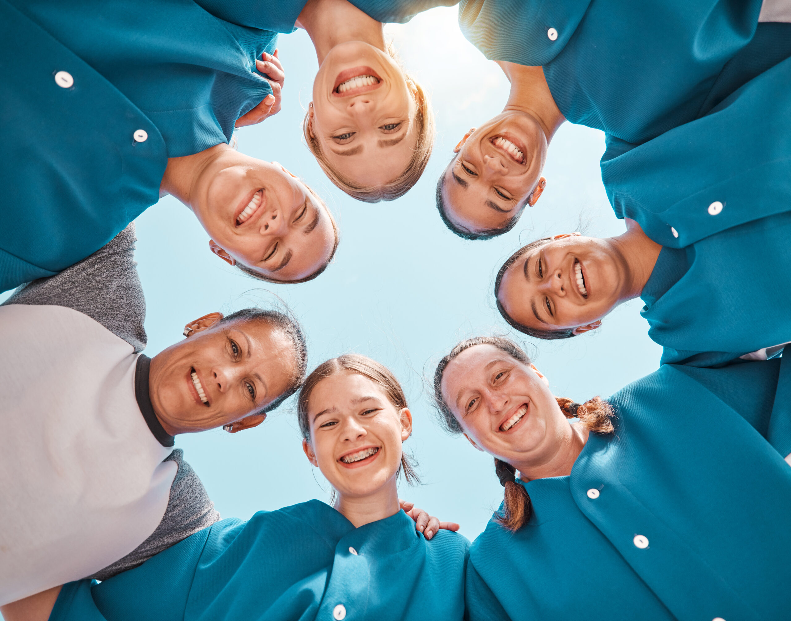 Smiling group of dental professionals standing in a circle, looking down at the camera against a blue sky.